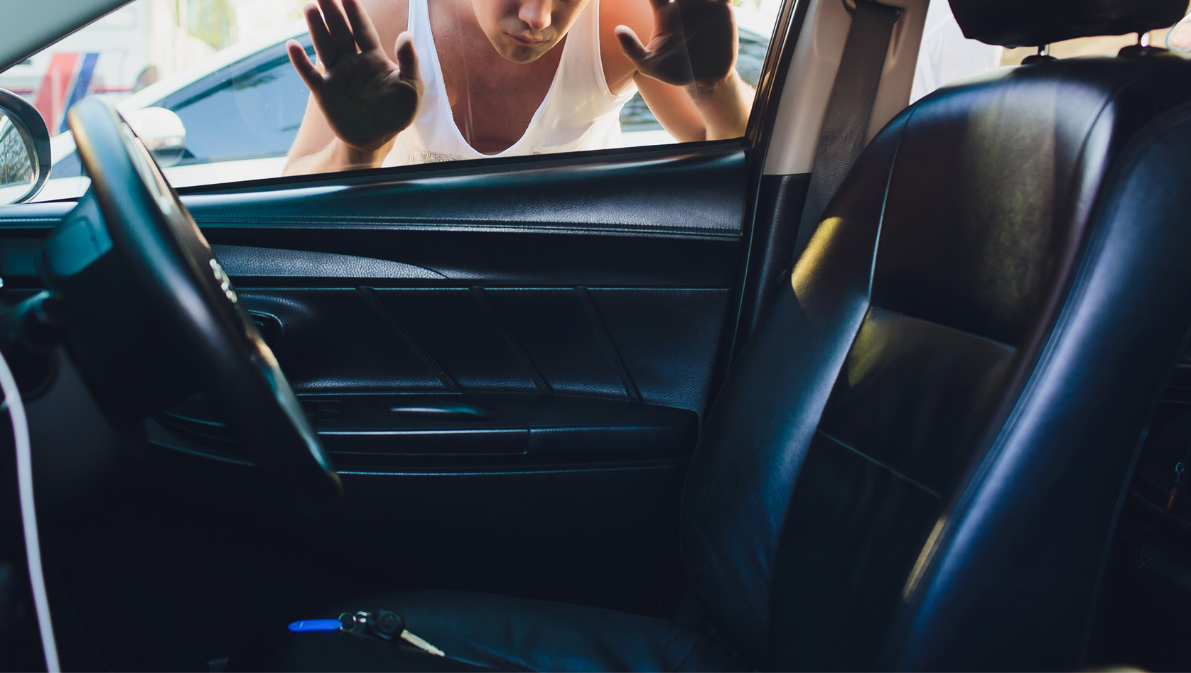 Image shows a person looking through their car window at keys on the seat. Image depicts vehicle lockout